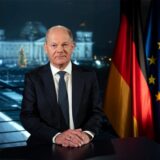 Bundeskanzler Olaf Scholz (SPD) sitzt während eines Fototermins nach der Aufzeichnung seiner Neujahrsansprache im Kanzleramt vor der Kulisse des von Scheinwerfern angestrahlten Reichstages.