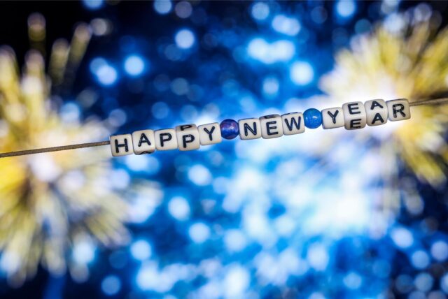 Der Schriftzug „Happy New Year“ (Frohes Neues Jahr) aus Buchstabenwürfeln hängt vor dem Foto eines Feuerwerks auf einem Computerbildschirm.