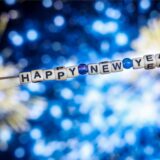 Der Schriftzug „Happy New Year“ (Frohes Neues Jahr) aus Buchstabenwürfeln hängt vor dem Foto eines Feuerwerks auf einem Computerbildschirm.