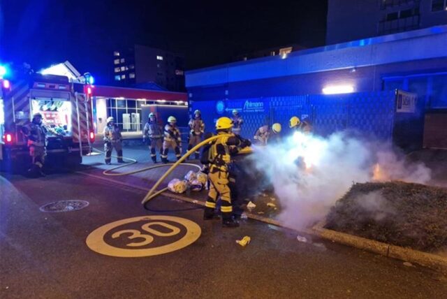 Ein Feuerwehrmann hält einen Schlauch auf brennendes Altpapier.