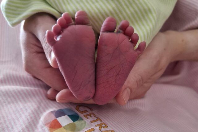 Eine Frau hält im Christlichen Klinikum Unna die Füße eines neugeborenen Babys in die Kamera, das in eine Decke gewickelt ist