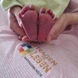 Eine Frau hält im Christlichen Klinikum Unna die Füße eines neugeborenen Babys in die Kamera, das in eine Decke gewickelt ist