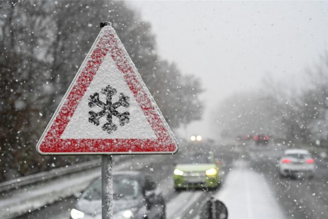 Ein Verkehrschild an der Südring-Brücke warnt vor Gefahr von Schnee- oder Eisglätte auf der Fahrbahn, während Schnee fällt.