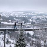Spaziergänger gehen über den Skywalk neben der Bobbahn mit Blick auf die Landschaft im Schnee.
