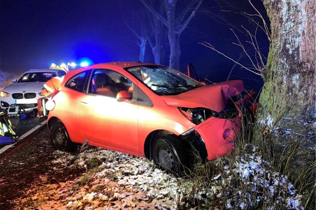Ein Wrack eines Autos steht frontal vor einem Baum.
