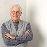 Der Unnaer CDU-Fraktionsvorsitzende Rudolf Fröhlich steht mit verschränkten Armen in der Ecke eines weiß gestrichenen Raumes.