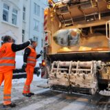 Zwei Müllwerker werfen Müllsäcke in ein Müllfahrzeug.