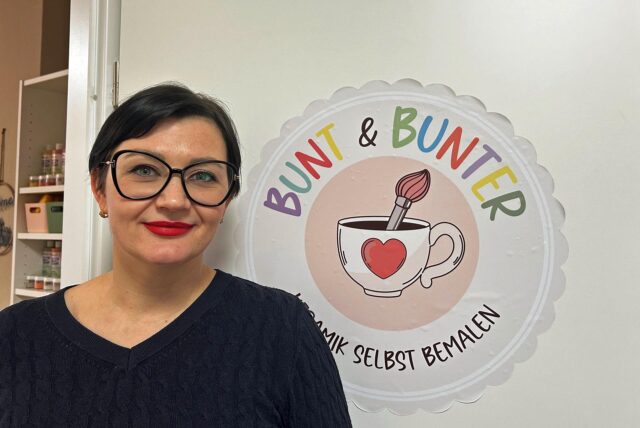 Tanja Au steht in einer Tür auf der ein Logo mit der Aufschrift „Bunt & Bunter Keramik selbst bemalen“ prangt.