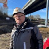 Mann mit Bauhelm vor Brücke.