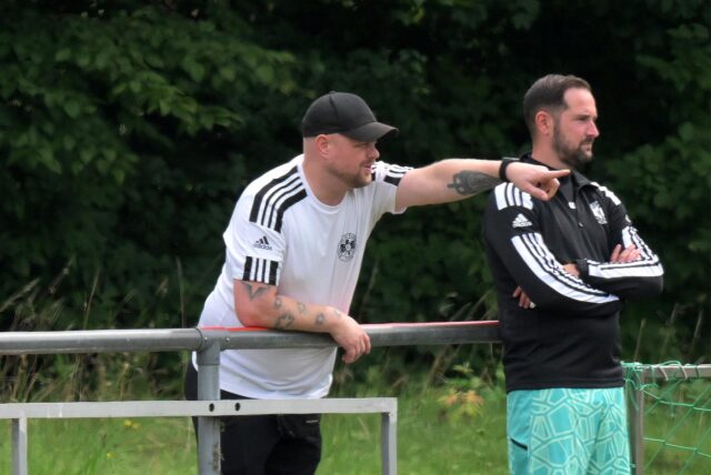 Stephan Ahland zeigt auf das Spielfeld, Sebastian Treppe steht daneben.
