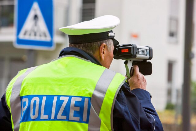 Ein Polizist kontrolliert mit einer Laserpistole die Geschwindigkeit auf einer Straße.
