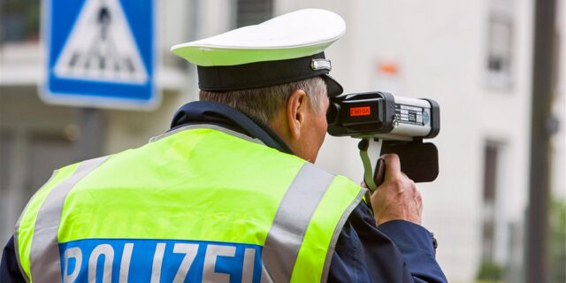 Ein Polizist kontrolliert mit einer Laserpistole die Geschwindigkeit auf einer Straße.
