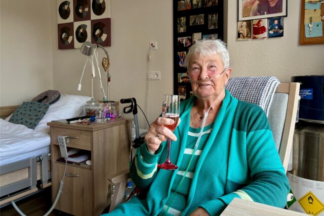 Uschi Pathmann aus Recklinghausen sitzt in einem Zimmer und trinkt aus einem Sektglas