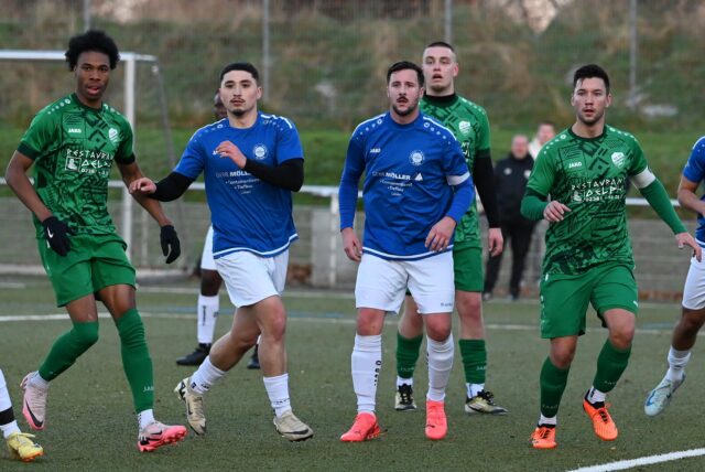 Fußballspieler zweier Mannschaften warten bei einer Standardsituation auf den Ball.