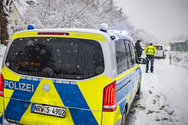 Ein Polizeiauto steht im Schnee hinter einem anderen Auto am Straßenrand.