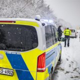 Ein Polizeiauto steht im Schnee hinter einem anderen Auto am Straßenrand.
