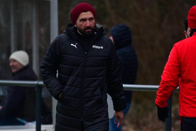Aykut Kocabas mit Winterjacke und Mütze an der Seitenlinie.