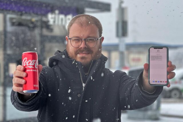Reporter Mathias Gaumann hält sein Handy und die gekaufte Cola Dose direkt in die Kamera und lächelt.