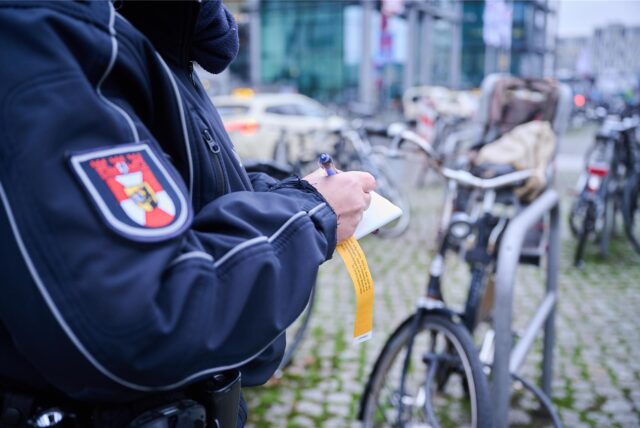 Eine Mitarbeiterin des Ordnungsamts in Berlin beschriftet einen gelben Hinweiszettel, der an einem Fahrrad befestigt wird.