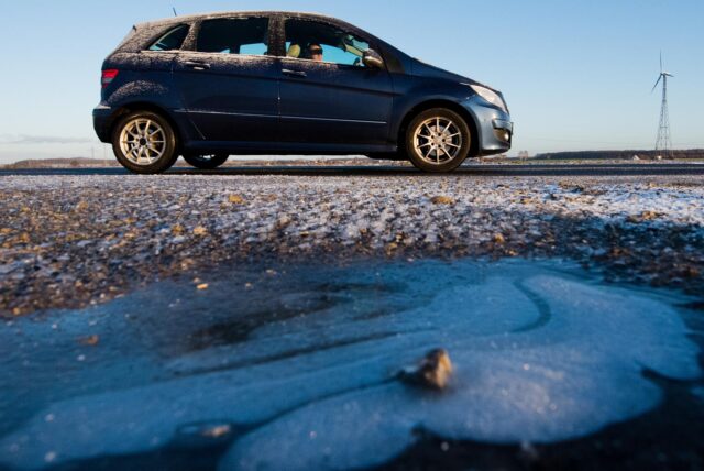 Ein Auto fährt über eine frostige Straße. Im Vordergrund ist eine zugefrorene Pfütze.