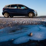 Ein Auto fährt über eine frostige Straße. Im Vordergrund ist eine zugefrorene Pfütze.