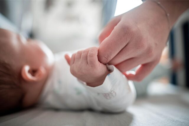 Ein Baby klammert sich an den Finger seiner Mutter.