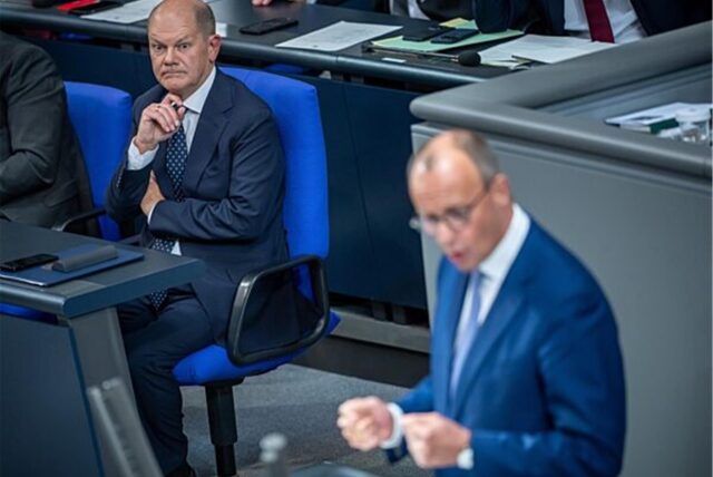Olaf Scholz schaut zu, während Friedrich Merz im Bundestag eine Rede hält.
