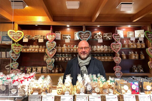 Der Inhaber Daniel Hein steht hinter der Theke seines Cafes. Die Theke ist gefüllt mit Keksen und Lebkuchenherzen.