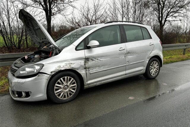Ein silberfarbenes Auto steht verschrammt und mit geöffneter Motorhaube  am Rand der Autobahn 1.