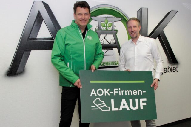 Jörg Kock (AOK-Serviceregionsleiter) und Marcus Hoselmann (upletics GmbH) halten ein Schild des AOK-Firmenlaufs hoch.