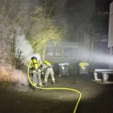 Feuerwehrleute löschen einen Mülleimerbrand.
