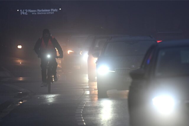 Fahrräder und Autos fahren am Morgen durch den Nebel.