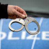 Eine Hand hält Handschelle, im Hintergrund ein Polizeiauto.