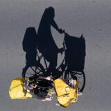 Ein Postbote auf einem Fahrrad wirft einen langen Schatten auf eine Straße.