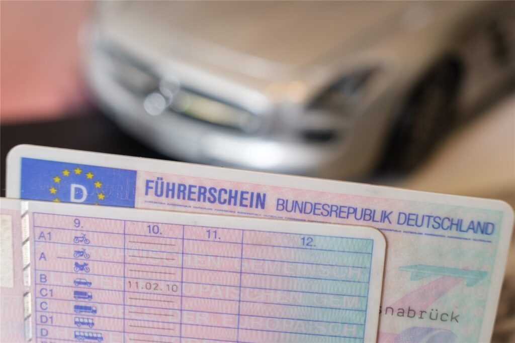 Zwei Führerscheine liegen vor einem Modellauto auf einem Tisch (gestellte Szene). 