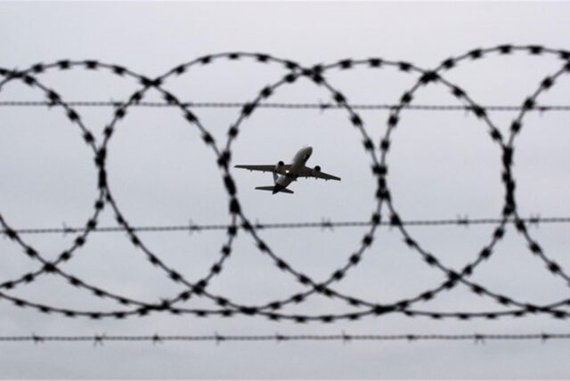 Ein Flugzeug startet – fotografiert durch einen Stacheldraht an einem Flughafenzaun