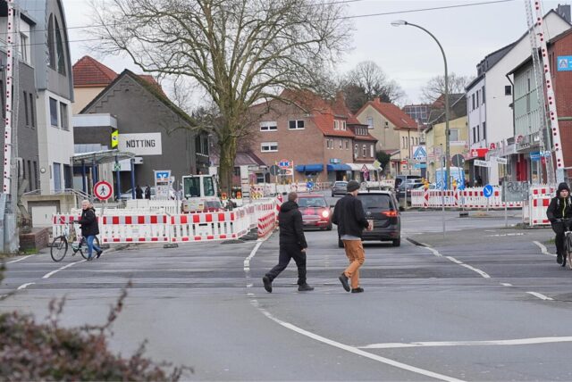 Menschen laufen über die Bahnhofstraße in Bönen. Im Hintergrund sieht man Baustellenbaken und einen Bagger.