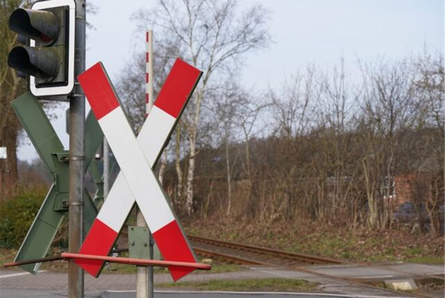 Blick auf einen Bahnübergang mit Andreaskreuzen, Ampeln und den Bahngleisen.