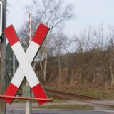 Blick auf einen Bahnübergang mit Andreaskreuzen, Ampeln und den Bahngleisen.