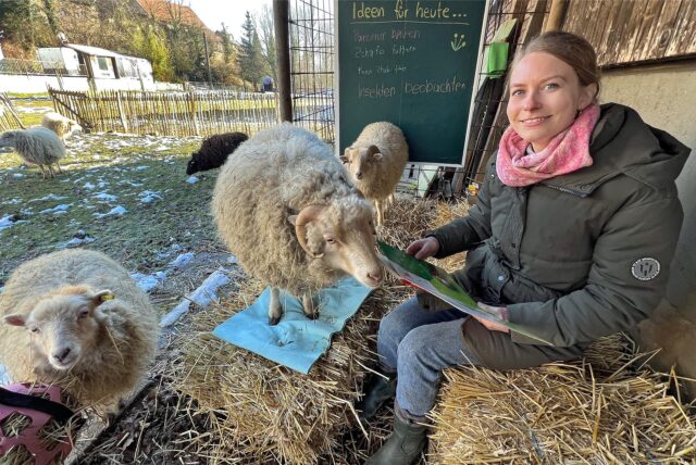 Johanna Röttger sitzt auf einem Strohballen. Neben ihr sind Schafe zu sehen.
