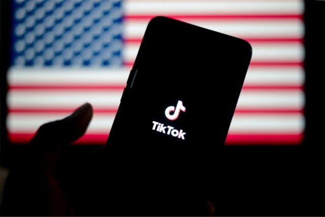 Ein Smartphone, auf dem die App Tiktok lädt – im Hintergrund die Flagge der USA