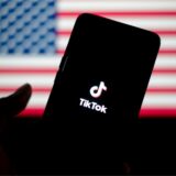 Ein Smartphone, auf dem die App Tiktok lädt – im Hintergrund die Flagge der USA
