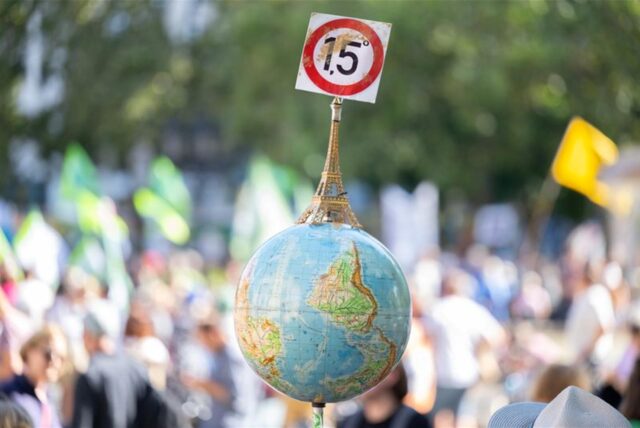Einen Globus mit einem Miniatur-Eiffelturm und dem 1,5-Grad Ziel des Pariser Klimaschutzabkommens trägt ein Mann auf der Demonstration vor der Alten Oper in Frankfurt.