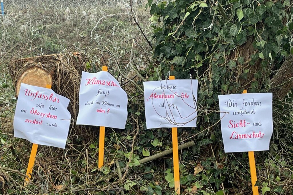 Protestplakate stehen vor einem Baum.