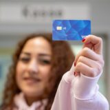 Eine Frau zeigt eine Musterkarte einer sogenannten Bezahlkarte für Geflüchtete.