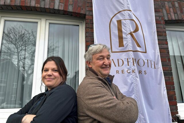 Christina Niehüser und Markus Reckers stehen vor der Flagge des neun Stadthotel Reckers in Werne.
