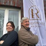 Christina Niehüser und Markus Reckers stehen vor der Flagge des neun Stadthotel Reckers in Werne.