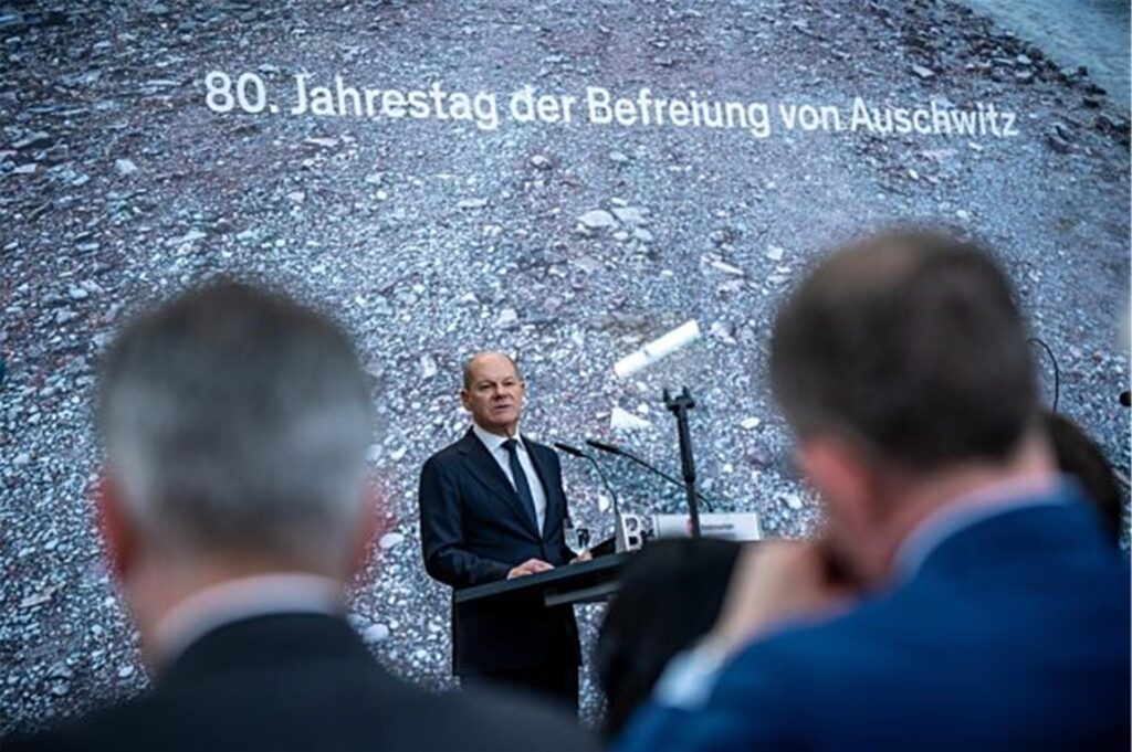 Olaf Scholz hält eine Rede. Auf der Leinwand hinter ihm auf der Bühne steht: 80. Jahrestag der Befreiung von Auschwitz.