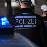 Das Logo der Polizei auf der Dienstkleidung von Polizisten die vor einem Blaulicht stehen
