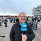Mathias Gaumann, Reporter des Hellweger Anzeigers, steht mit Mikron in der Marina Rünthe. Im Hintergrund sind Besucher des Hafenfeuers 2025 zu sehen.